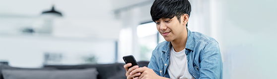 Young male sitting and smiling while holding his phone 